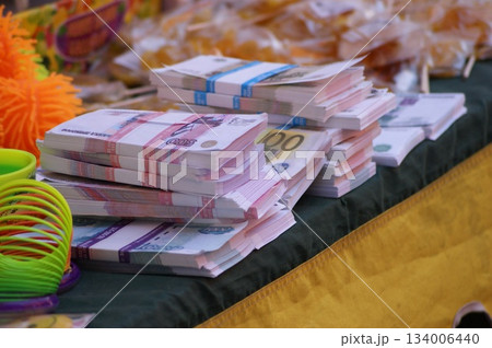 The photograph shows stacks of money neatly arranged on a table. The money is of various denominations, including 100- and 500-euro bills. Colorful jewelry and other objects are visible in the backgro 134006440