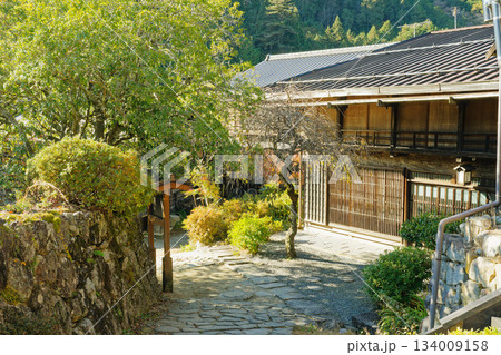 石畳の小径と庭木に囲まれた木造町家の玄関先・妻籠宿の落ち着いた町並み 134009158