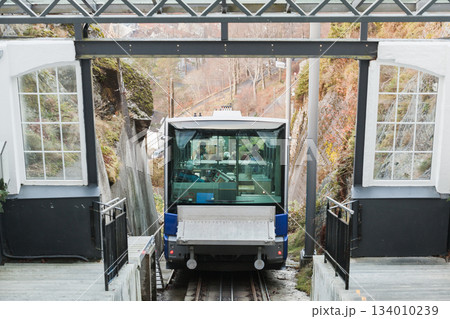 A modern cable car enters a glass-walled station, passengers visible inside A modern cable car enters a glass-walled station, passengers visible inside 134010239