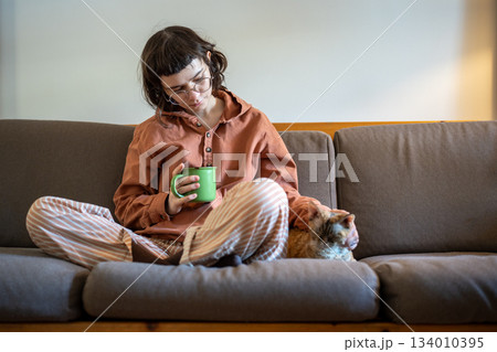 Loving teenager spending time at home with beloved cat Devon Rex, sitting on couch, drinking tea 134010395