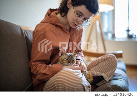 Teen girl stroking petting cat from shelter sits on sofa at home. Anti stress pet therapy, cat lover Teen girl stroking petting cat from shelter sits on sofa at home. Anti stress pet therapy, cat lover 134010420