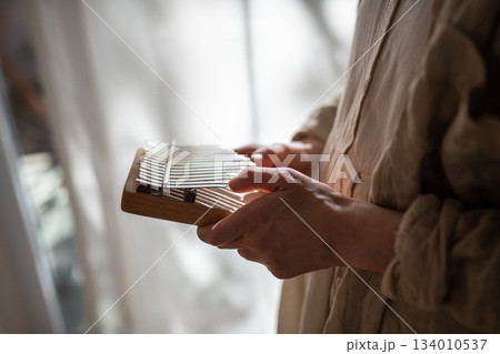 Woman hands studying to play music on wooden kalimba standing near window at home. Woman hands studying to play music on wooden kalimba standing near window at home. 134010537