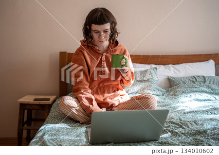 Girl watching series movie on laptop sits in bed drink tea at home leisurely passing time on day off Girl watching series movie on laptop sits in bed drink tea at home leisurely passing time on day off 134010602