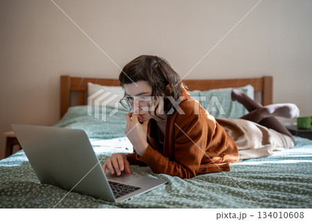 Concentrated teen girl reading book online, scrolling social networks in internet on laptop computer Concentrated teen girl reading book online, scrolling social networks in internet on laptop computer 134010608