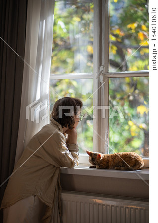 Melancholic pet owner looking at window in depression while staying at home in sunny summer day Melancholic pet owner looking at window in depression while staying at home in sunny summer day 134010610