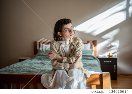 Pensive teen sitting on bed, looking at window, thinking of misunderstanding with friends, parents Pensive teen sitting on bed, looking at window, thinking of misunderstanding with friends, parents 134010614