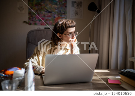 Dreamy teenager looking at window during work break, thinking of going for walk in sunny weather Dreamy teenager looking at window during work break, thinking of going for walk in sunny weather 134010650
