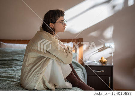 Depressed tired teenage girl sitting on bed sadly looking at window feeling apathy frustration.  134010652