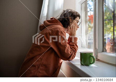 Introverted teen girl standing near window, looking at street indifferently, thinking of life 134010684