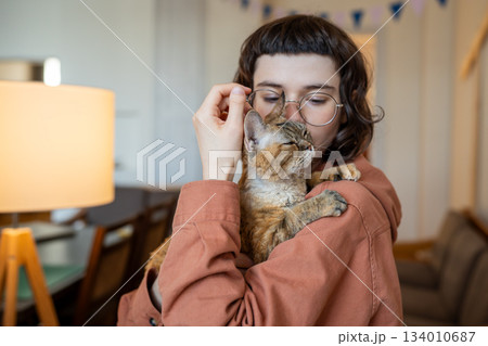 Cat owner caring woman hug kissing holding in hands loving pet at home. Therapy by domestic animal 134010687