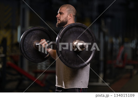 man is lifting a barbell while doing a bicep curl in a gym setting. The workout takes place in the morning. He focuses on strength training to improve fitness. man is lifting a barbell while doing a bicep curl in a gym setting. The workout takes place in the morning. He focuses on strength training to improve fitness. 134015109