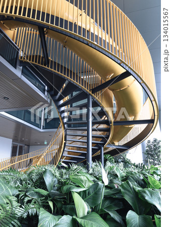 A vibrant fusion of bold architecture and nature unfolds with a striking yellow spiral staircase at its center, beautifully encircled by lush greenery." 134015567
