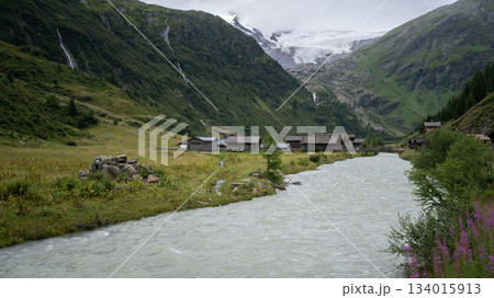 Alpine village scenery with glacial river flowing through and massive glacier above, Austrian Alps Alpine village scenery with glacial river flowing through and massive glacier above, Austrian Alps 134015913