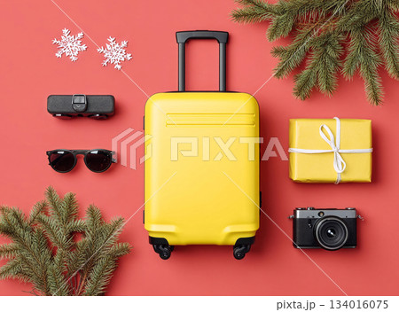 Bright yellow suitcase and holiday items arranged on red background, showcasing travel essentials for festive season adventures 134016075