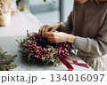 Crafting a beautiful holiday wreath with fresh greenery and decorative berries in a cozy space during winter season 134016097