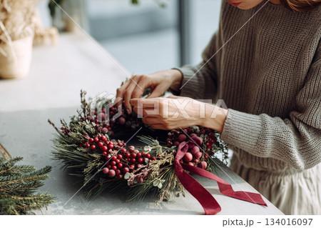 Crafting a beautiful holiday wreath with fresh greenery and decorative berries in a cozy space during winter season Crafting a beautiful holiday wreath with fresh greenery and decorative berries in a cozy space during winter season 134016097