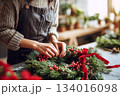 Creating a beautiful Christmas wreath with natural greens and red berries in a cozy workshop during the holiday season 134016098