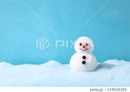 Cute snowman with a cheerful smile stands on soft snow against a bright blue background during winter Cute snowman with a cheerful smile stands on soft snow against a bright blue background during winter 134016102