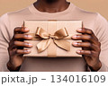 Hands hold a beautifully wrapped gift with a bow against a neutral background, perfect for celebrating special occasions 134016109