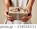 Present wrapped in brown paper held by hands with elegantly tied ribbon in a neutral-toned setting 134016111