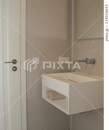 Minimalist bathroom interior with a floating white sink, neutral ceramic tiles, and clean contemporary lines. Soft lighting and functional design highlight modern home decor, renovation themes, and 134016643