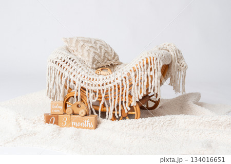 Soft nursery decor arrangement with knitted blanket, textured pillow and wooden toy sleigh on a fluffy surface. Warm neutral tones create a calm atmosphere suited for baby room styling, interior 134016651