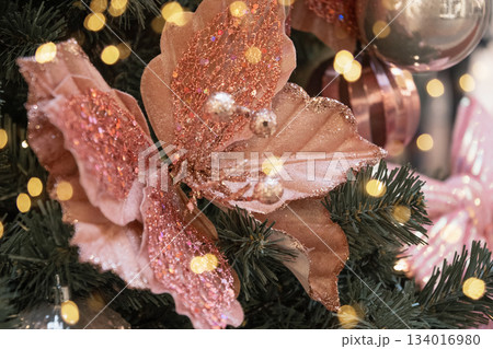 Pink glitter creative flower Christmas decoration on fir tree with warm festive lights. Elegant holiday ornament with soft bokeh background. Pink glitter creative flower Christmas decoration on fir tree with warm festive lights. Elegant holiday ornament with soft bokeh background. 134016980