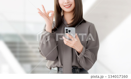 スマートフォンを持ってOKポーズをする笑顔の女性・ビジネスウーマン スマートフォンを持ってOKポーズをする笑顔の女性・ビジネスウーマン 134017160
