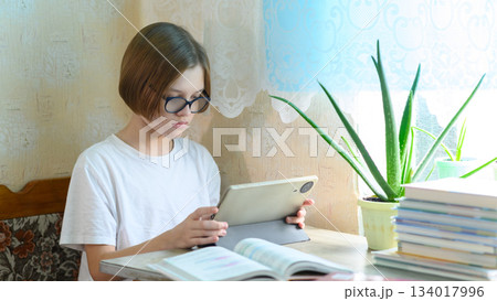 teen boy in glasses studying with a tablet at the desk 134017996
