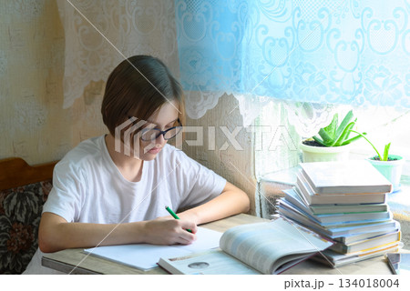 student in glasses writing with a pen in a notebook at home 134018004