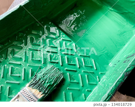 Green paint filling textured tray with paintbrush soaking in vibrant color, ready for diy projects, home improvement or creative art and craft work. Decorative for design 134018729