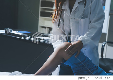 Doctor examining and supporting injured ankle of female patient in hospital room, providing medical assistance and treatment for sprain or fracture Doctor examining and supporting injured ankle of female patient in hospital room, providing medical assistance and treatment for sprain or fracture 134019332