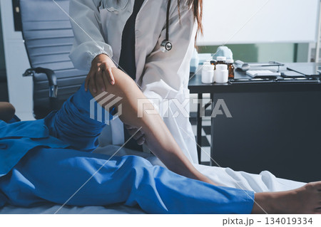 Doctor examining and supporting injured ankle of female patient in hospital room, providing medical assistance and treatment for sprain or fracture Doctor examining and supporting injured ankle of female patient in hospital room, providing medical assistance and treatment for sprain or fracture 134019334