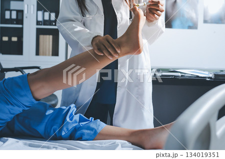 Doctor examining and supporting injured ankle of female patient in hospital room, providing medical assistance and treatment for sprain or fracture Doctor examining and supporting injured ankle of female patient in hospital room, providing medical assistance and treatment for sprain or fracture 134019351