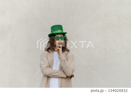 Man wearing Shamrock clover glasses and Green St. Patrick's Hat against beige wall. Space for design. Man wearing Shamrock clover glasses and Green St. Patrick's Hat against beige wall. Space for design. 134020832