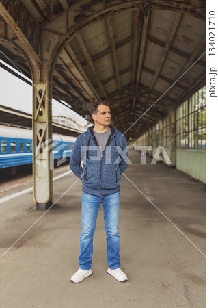 Tanned, middle-aged, brunette man of Spanish or Brazilian appearance in casual clothes stands at train station and looks away Tanned, middle-aged, brunette man of Spanish or Brazilian appearance in casual clothes stands at train station and looks away 134021710