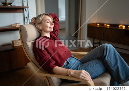 Peaceful middle aged woman with closed eyes and happy expression relaxing in comfy chair at home. Peaceful middle aged woman with closed eyes and happy expression relaxing in comfy chair at home. 134022361