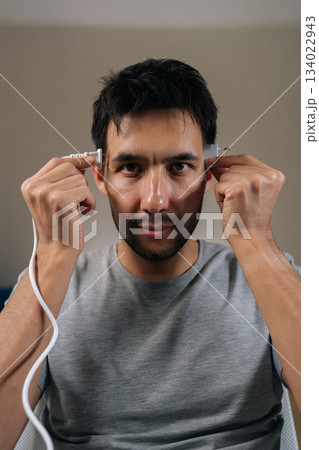Vertical portrait of young man plugs electrical connectors into temples, symbolizing activation of brainpower, creative energy and technological intelligence for innovative problem-solving and ideas. Vertical portrait of young man plugs electrical connectors into temples, symbolizing activation of brainpower, creative energy and technological intelligence for innovative problem-solving and ideas. 134022943