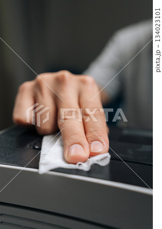 Detail cropped shot of man performing printer maintenance, wiping dust off office laser printer, ensuring technology hygiene, cleaning and servicing electronic equipment in home office. 134023101