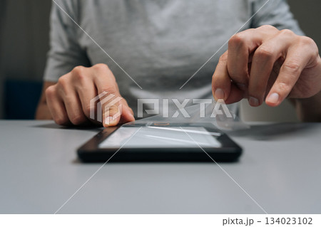 Close-up hands of unrecognizable man removing clear screen protector from onto portable e-reader device, ensuring electronic book display is protected from scratches and everyday wear. 134023102