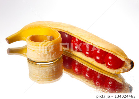 Surreal food composition of a peeled banana filled with glossy cherry tomatoes 134024465