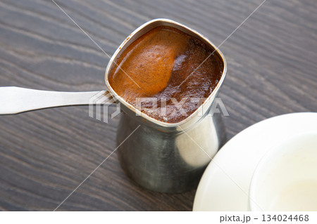 Rustic image of a metal cezve holding aromatic Turkish coffee on a wooden background. Rustic image of a metal cezve holding aromatic Turkish coffee on a wooden background. 134024468