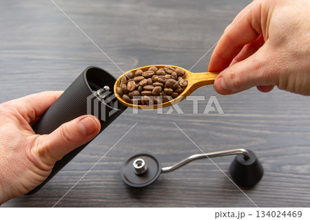 Close-up of hands using a black coffee grinder and a wooden spoon Close-up of hands using a black coffee grinder and a wooden spoon 134024469