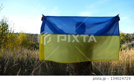 Military man in uniform stands with raised over head flag of Ukraine at countryside. Male ukrainian army soldier with lifted national banner in honor of victory against russian aggression. End of war 134024729