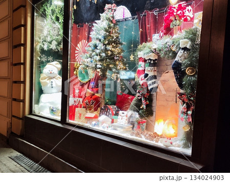 Festive shop window display decorated Christmas tree with lights and ornaments. Gifts in colorful wrapping are arranged below 134024903