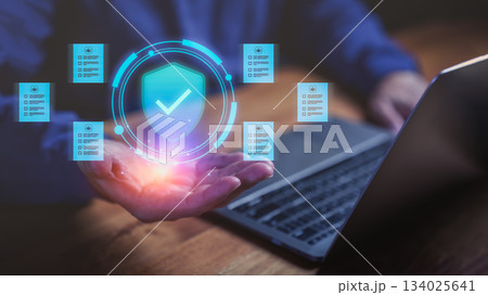 Businessman using laptop with holographic shield icon and digital documents, symbolizing data protection, cybersecurity, privacy policy, compliance, and secure information management. 134025641