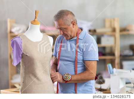 Male tailor standing in workshop checking dress Male tailor standing in workshop checking dress 134026175