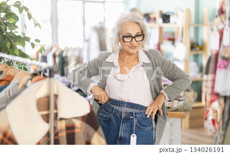 Mature woman standing in store and choosing jeans Mature woman standing in store and choosing jeans 134026191