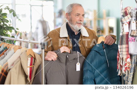 elderly man carefully chooses a down jacket in a store elderly man carefully chooses a down jacket in a store 134026196