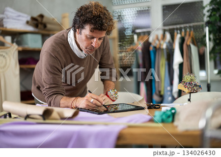 Man tailor creates sketch of dress on tablet 134026430